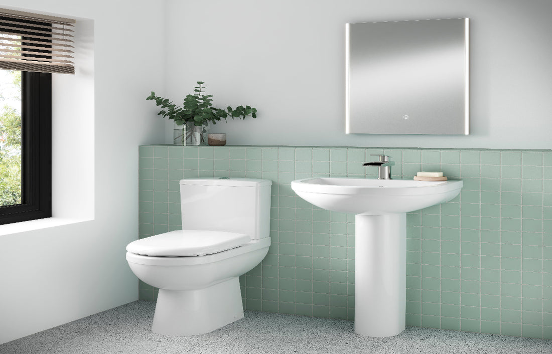 Bathroom with a white sink and toilet against a green tiled wall.