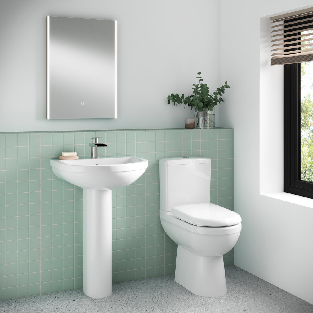 Bathroom with a white sink and toilet against a green tiled wall.