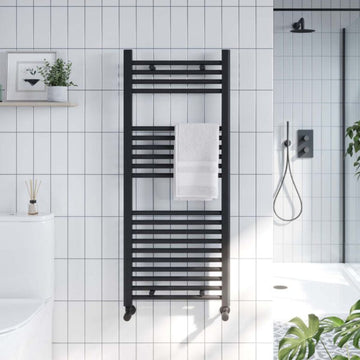 Black towel radiator mounted on a tiled bathroom wall with a white bathtub and shower in the background.