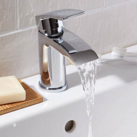 Chrome faucet with water flowing into a sink, soap on a wooden dish.